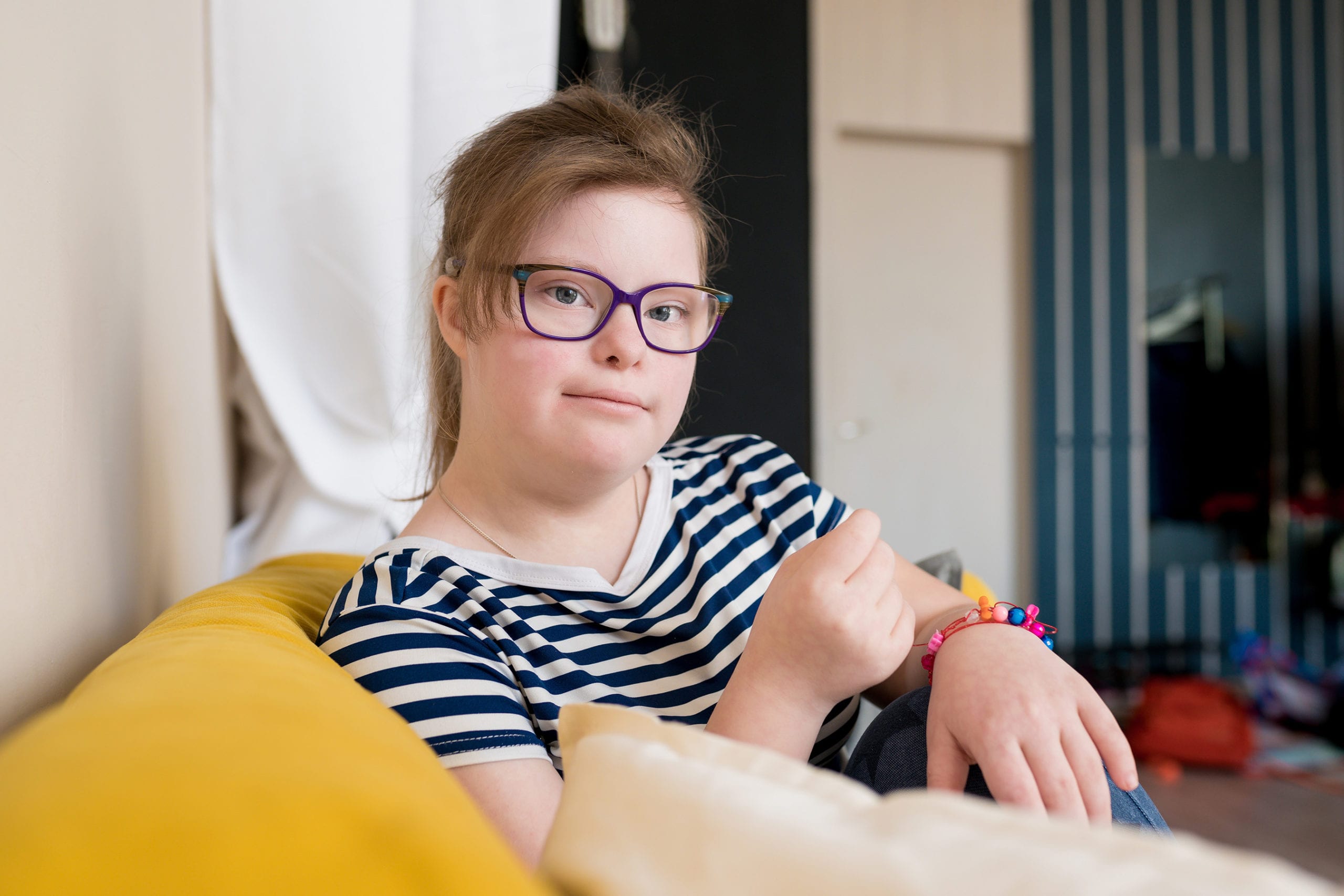 Portrait of cute teenager girl with Down syndrome sitting on sof