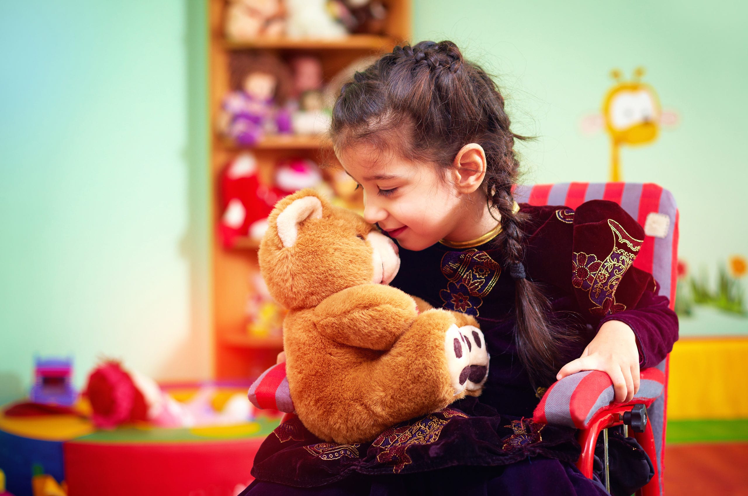 cute little girl in wheelchair hugging plush bear in kindergarten for kids with special needs